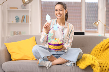 Young woman with basket of Easter eggs sitting on sofa at home