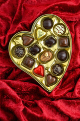 Happy Valentine’s Day, gold heart shaped box of assorted chocolate candy on luxurious red velvet background
