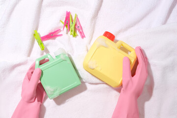 Hands wearing pink rubber gloves are holding two bottles of detergent and clothespins that stand...