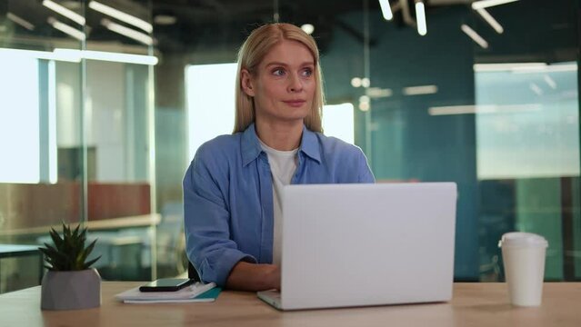 Smiling young woman typing at pc keyboard and looking away with playful smile while sitting indoor. Pleased manager conducting business correspondence while remembering rules of formal communication.