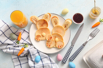 Fototapeta na wymiar Funny Easter bunny pancakes with glass of orange juice and painted eggs on light blue background