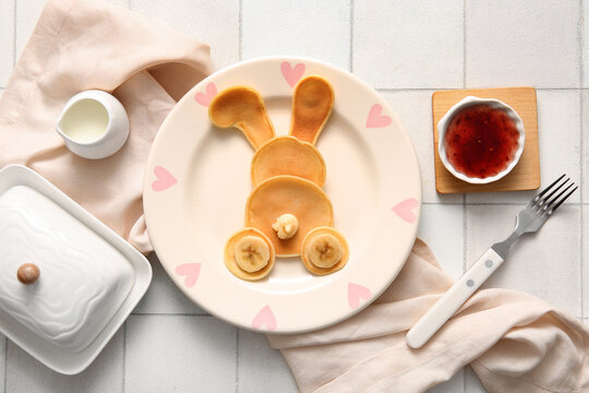 Funny Easter bunny pancakes with milk and jam on white tile background