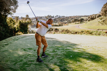 Sotogrante, Spain - January 25, 2024 - Golfer at the end of a swing on a tee box, with a golf course and hilly landscape in the background.
