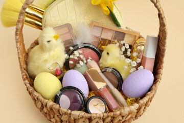 Wicker basket with decorative cosmetics, baby chickens and Easter eggs on beige background, closeup