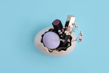 Basket in shape of Easter egg with lipsticks and flowers on blue background
