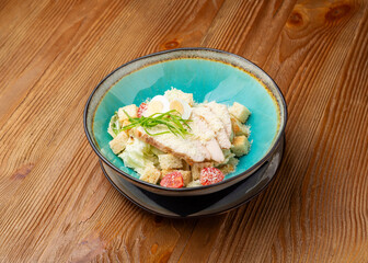 Caesar salad with chicken in a plate on a wooden background
