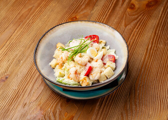 Caesar salad with shrimp in a plate on a wooden background