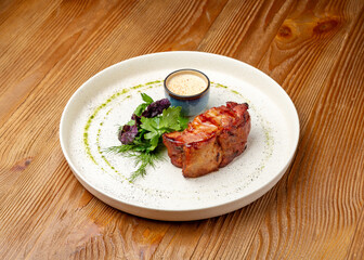 Baked pork with mustard sauce in a plate on a wooden background