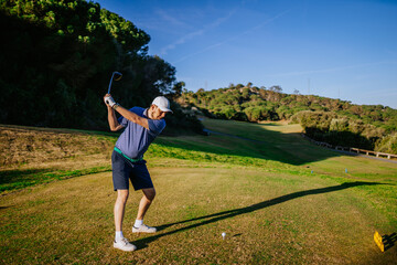 Sotogrante, Spain - January 25, 2024 - Man mid-swing at a golf ball on a course with trees and a clear sky.