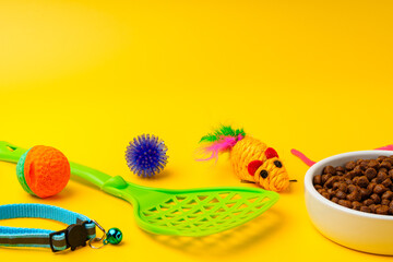 Cat bowl with dry food and toys on yellow background studio shot