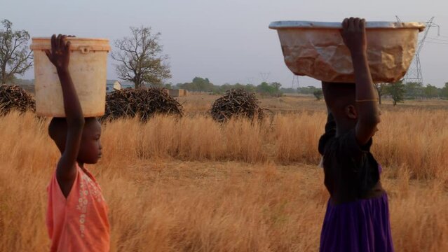 established of african people child kids carrying water in bucket over their head with rural background of Africa