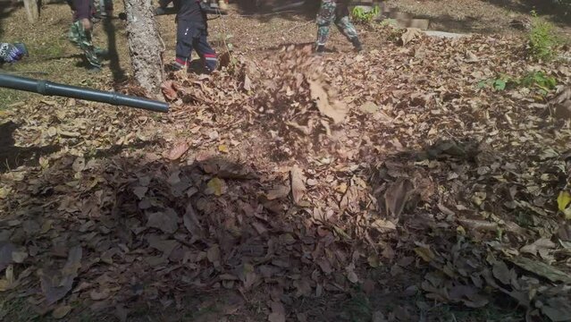 Slow motion Gardeners simultaneously use a backpack blower. .Blow the leaves and grass clippings together into a large pile. .Keep your garden clean and prevent forest fires. clean park background.