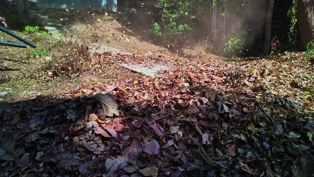 Slow motion Gardeners simultaneously use a backpack blower. .Blow the leaves and grass clippings together into a large pile. .Keep your garden clean and prevent forest fires. clean park background.