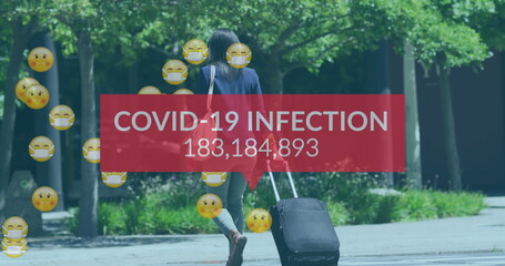 Image of covid 19 infection numbers end emojis over woman with suitcase wearing face mask
