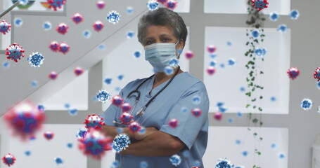 Image of covid 19 cells over female doctor wearing face mask