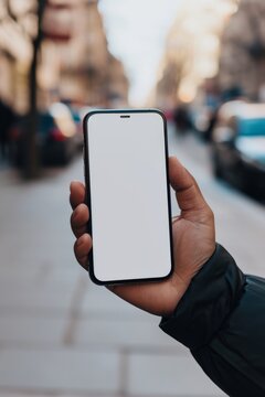 Mockup image of a male hand holding a smartphone with a blank screen on the background of a city street