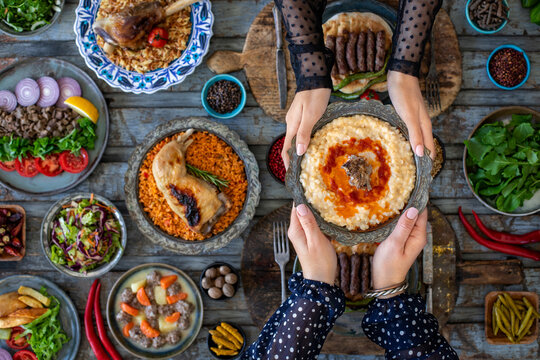 Hands of two women holding tradiitional meal harries or keşkek at the dining table with many meals. A meal with wheat and meat. 