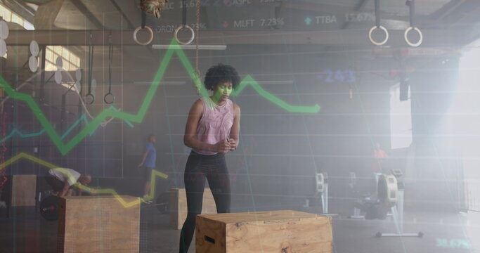 Image of graph processing over biracial woman jumping on box cross training at gym