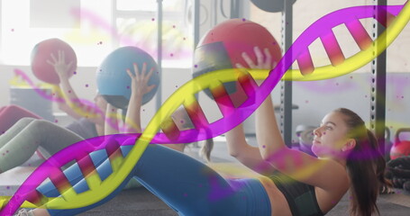 Image of dna strands over diverse women cross training with medicine balls at gym