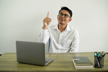 young asian businessman in a workplace pointing up and surprised, wearing white shirt with glasses isolated