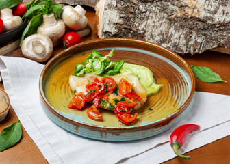 Tilapia fish with vegetables in a plate on a wooden background