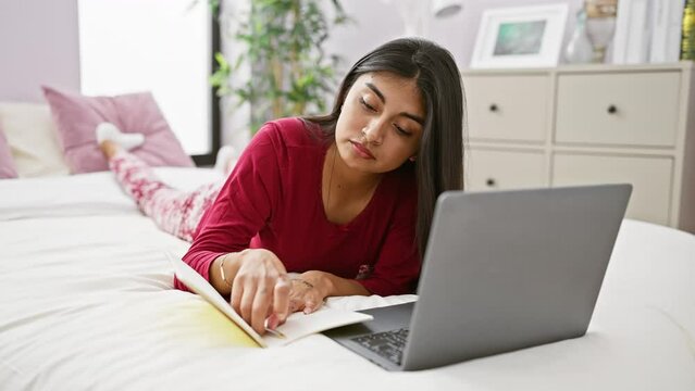 Indian woman working on laptop in bedroom, lying on bed with notebook, focused, comfortable, technology, indoor.