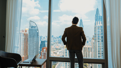 Back view ambitious businessman standing in ornamented office gazing out window to cityscape skyline. Determination and business ambition drive business career toward to bright future - obrazy, fototapety, plakaty
