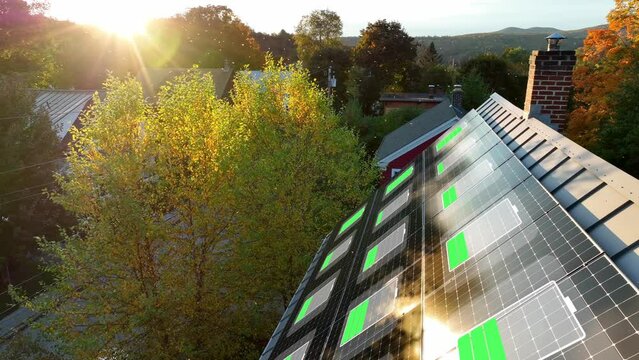 Solar panels featuring a battery charging animation. Autumn sunrise with colorful foliage. Sloped metal roof of American home with solar energy array.