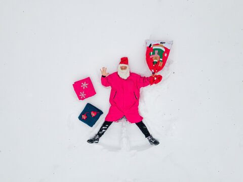 joyful santa claus in a vibrant pink suit lying in the snow, surrounded by colorful christmas gifts and a festive stocking, celebrating the winter season's happiness and holiday spirit