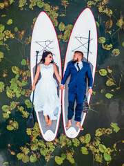 aerial view of a couple in wedding attire lying on a paddleboard amidst lily pads, celebrating love...