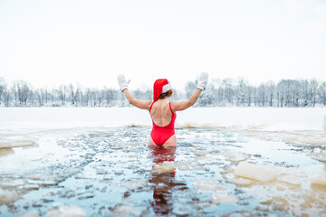 joyful winter swimmer in santa hat celebrating in icy water with arms raised - festive and brave...