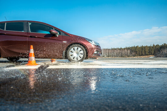 dynamic car braking test on wet road surface with water splashes and orange traffic cones, vehicle safety evaluation in controlled skidpan environment