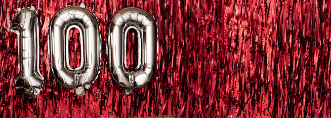 Silver foil balloon number, digit one hundred on red background. Birthday greeting card with...