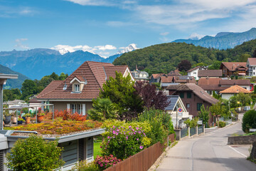 Fototapeta na wymiar Street view of beautiful houses with flowers and greenery, mountains in the background, the town of Spiez, Swiss Alps, Switzerland. ​