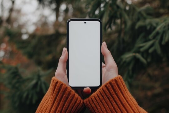 Mockup image of a woman's hands holding a smartphone with a white screen in the park