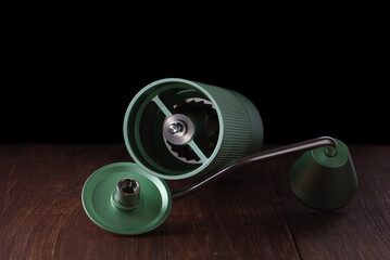 Green manual coffee grinder with metal millstones is open on a wooden table.