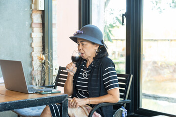 Asian elderly woman drinking wine watching online movie or video call friends or family, senior...