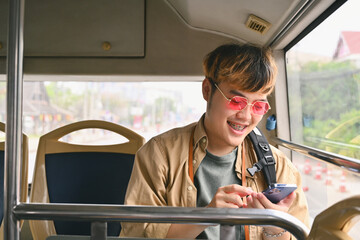 Happy smiling man sitting on a bus seat as a travel passenger and using mobile phone