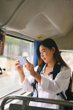 Smiling young woman taking photos trough the window with smartphone.Travel and transportation concept