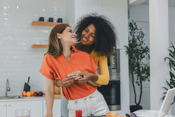 Multiethnic lesbian couple having embracing in kitchen room. black and white couple holding ring....