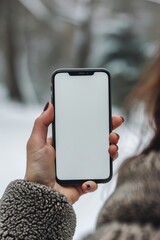 Mockup image of a female hand holding a smartphone with a blank white screen in the winter park