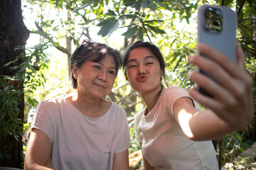 Asian Thai daughter and elder mother taking selfie together with happiness, while spending time together at cafe in garden on holidays.