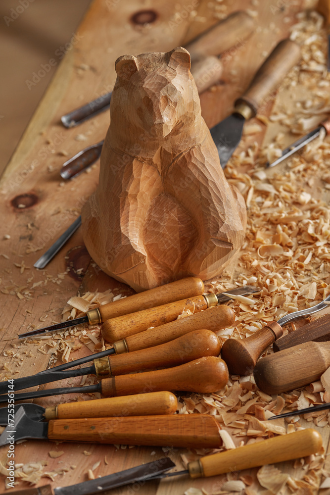 Wall mural Wood carving, Unfinished bear sculpture emerges under warm illumination. Carving tools and wood shavings trace the skilled animalist's transformative process