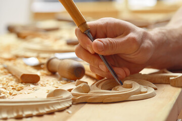 Image documenting woodcarving process: male hand utilizing chisel to create elaborate floral design...