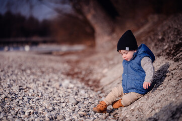 Curious toddler sitting on pebbles by the lake, exploring with a focused expression