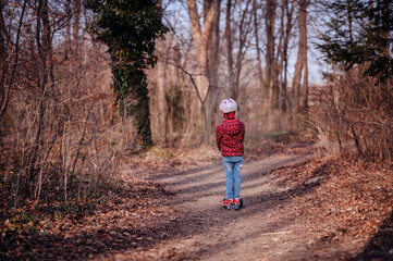 Fototapeta premium Child in a helmet focused on riding a scooter along a forest trail, adventure time outdoors