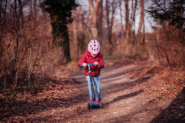 Naklejka na ściany i meble Child in a helmet focused on riding a scooter along a forest trail, adventure time outdoors