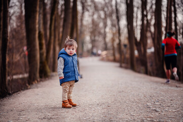Fototapeta premium Curious Toddler's Winter Walk. A young child in a warm vest wanders a forest path, curiosity in his eyes