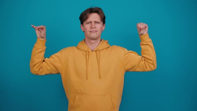Young man shows bla-bla-bla gesture. Guy in yellow jacket imitates talking with hand, standing on blue background in studio. Babbling.