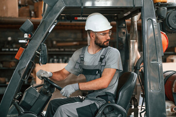 Fototapeta na wymiar Driving the forklift. Young factory worker in grey uniform
